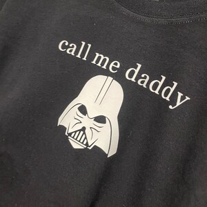 Op de afbeelding: Zwart T-shirt met een witte afbeelding van Darth Vaders hoofd en de tekst "call me daddy".