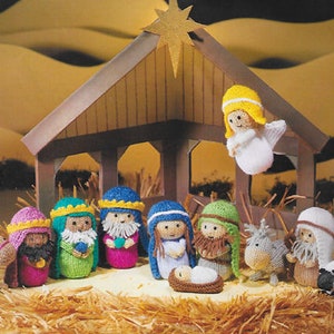 May include: A knitted nativity scene with figures including the Holy Family, wise men, an angel, and animals. The figures are brightly coloured, with details such as beards, crowns, and robes. The scene is set in a wooden stable with a star above.