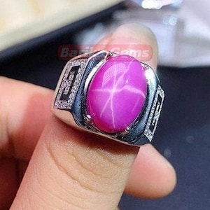 Peut inclure: Une bague en argent avec une pierre précieuse en saphir étoilé rose. La bague est ornée d'un motif décoratif autour de la pierre.