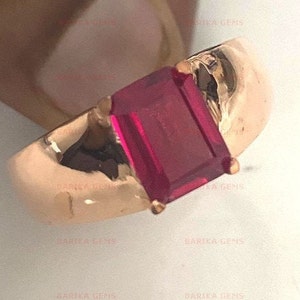 May include: A gold ring with a large, square-shaped, deep red gemstone. The ring is set in a simple, smooth band.