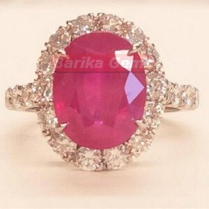 May include: A ring featuring a large oval ruby, surrounded by a halo of smaller diamonds. The ring is set in white gold.