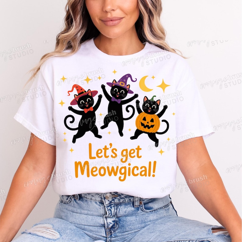 Puede incluir: Camiseta blanca con un dise&ntilde;o de Halloween. Presenta tres gatos negros con sombreros de bruja y un disfraz de calabaza. El texto "Let's get Meowgical!" est&aacute; impreso en naranja. El dise&ntilde;o incluye estrellas y una luna.