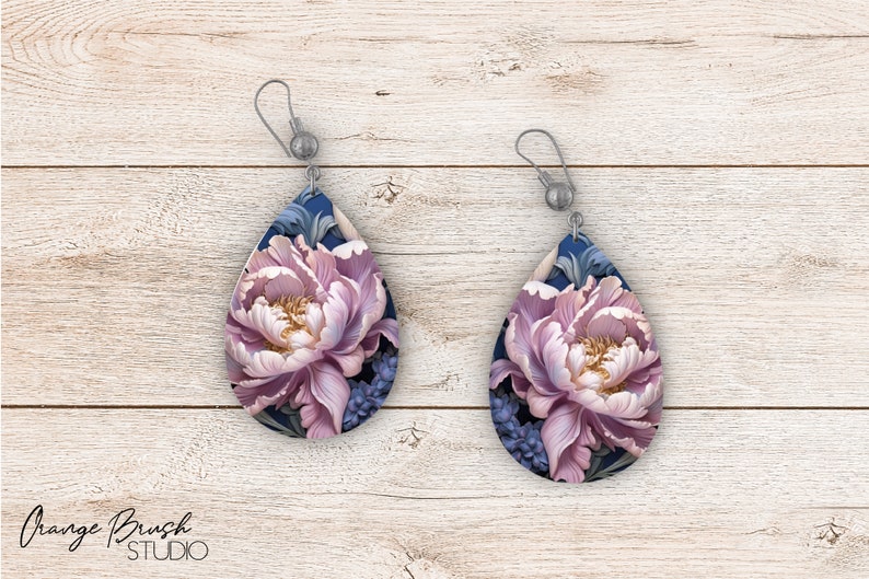 May include: A pair of teardrop-shaped earrings with a floral design. The earrings feature a pink peony flower with blue and green leaves on a dark blue background.