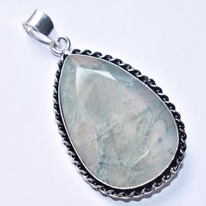 以下が含まれることがあります： 大きな淡い緑色の宝石が付いた、涙型のペンダント。石には内部の静脈があり、ねじれたロープのデザインの銀色の金属フレームにセットされています。ベイルもシルバーです。