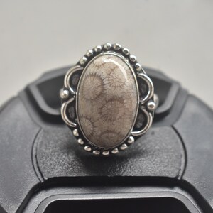 Op de afbeelding: Ovale ring met een lichtbruine steen met een uniek patroon, gezet in zilverkleurig metaal. De ring heeft een decoratieve rand met kleine, ronde accenten. Een sieraad.