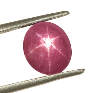 May include: A pink star ruby gemstone with a six-pointed star in the center, held by tweezers.