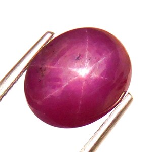 May include: A deep pink star ruby gemstone with a six-rayed star in the center. The ruby is oval shaped and is set in a silver tone setting.
