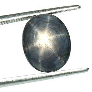 May include: A dark blue star sapphire gemstone with a star-like pattern in the center, held by a pair of tweezers.