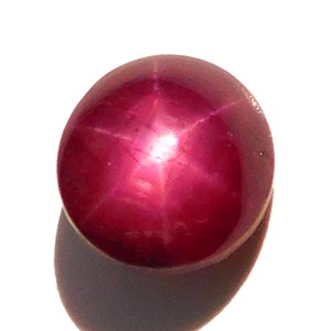 Può includere: Una pietra preziosa di rubino stellare rosso scuro con una stella a sei punte al centro.