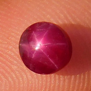 May include: A deep red star ruby gemstone with a six-pointed star in the center.