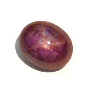 Peut inclure: Une pierre précieuse polie de forme ovale avec un effet d'étoile. La gemme présente une teinte rouge-violet profond avec un motif en étoile à six rayons visible sur sa surface. La pierre a une finition lisse et brillante.
