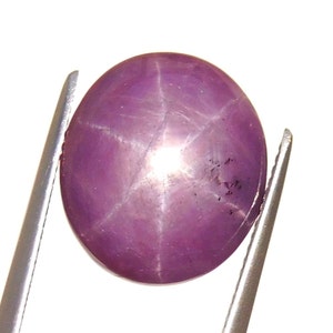 May include: A pink star sapphire gemstone with a six-rayed star in the center. The gemstone is round and cabochon cut.
