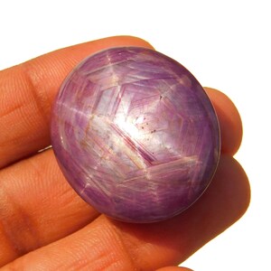 May include: A large, oval-shaped, purple star ruby gemstone with a six-pointed star in the centre.