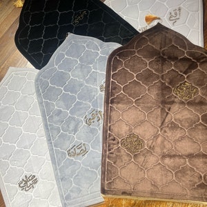 May include: Four prayer rugs with gold trim and intricate patterns. The rugs are in black, brown, and two shades of gray. Each rug has a different Arabic inscription in gold.