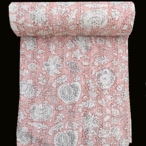 Op de afbeelding: Roze kantha-deken met een wit bloemenpatroon. De deken is opgerold en het bloemenpatroon is zichtbaar op de stof.