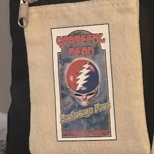 May include: A black and beige canvas bag with a zipper closure. The bag has a patch with the Grateful Dead logo and the text "Backstage Pass".