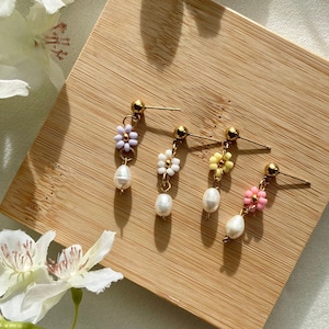 Könnte beinhalten: Vier Paar Hängeohrringe mit Perlen-Tropfen und Blumen-Anhängern. Die Blumen sind aus bunten Perlen gefertigt und in den Farben Lila, Gelb und Rosa gehalten.