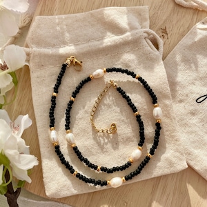 May include: A black beaded choker necklace with a gold clasp and white pearl accents.
