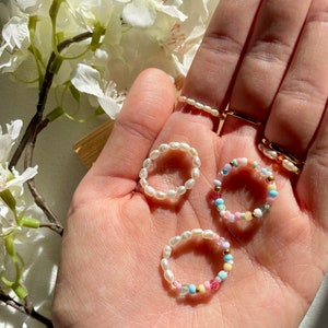 Könnte beinhalten: Drei Ringe mit unterschiedlichen Designs. Ein Ring ist aus weißen Perlen, ein anderer aus bunten Perlen und der dritte aus weißen und bunten Perlen.