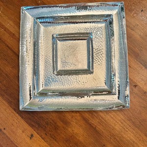 May include: A silver square serving tray with three concentric square frames. The tray has a hammered finish.