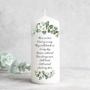 Op de afbeelding: Witte pilaarvormige kaars met een groen-wit bloemenontwerp en een gedicht dat luidt: "Degenen van wie we houden, Gaan niet weg, Ze lopen naast ons, Elke dag Onzichtbaar, onverhoord Maar altijd dichtbij, Nog steeds geliefd Nog steeds gemist En heel dierbaar."