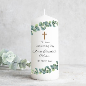 Könnte beinhalten: Weiße Taufkerze mit goldenem Kreuz und Eukalyptusblättern. Der Text lautet "On Your Christening Day Sloane Elizabeth Maher 11th March 2023".