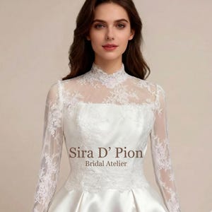 Bride wearing a long sleeve French lace bridal topper with sheer illusion neckline, floral lace embroidery, and elegant fitted styling over a white wedding gown