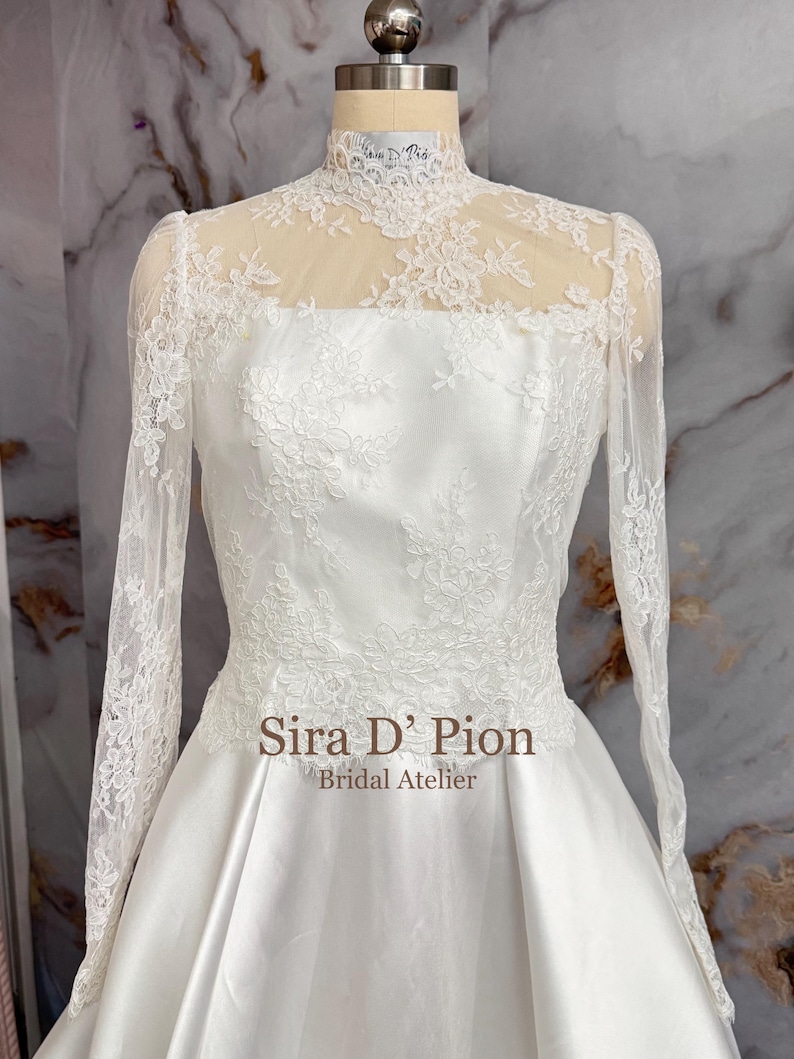 Beautiful wedding dress topper, Alecon Lace bridal topper, handcrafted in Florida. Highe neck, long sleeves and cover buttons. A white lace wedding dress bodice with a high neck and long sleeves. The lace is delicate and features floral patterns.