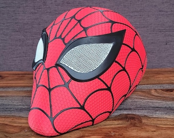 Puede incluir: Una máscara de Spider-Man roja y negra con una cubierta de ojo de malla. La máscara tiene una superficie texturizada y un diseño de telaraña.