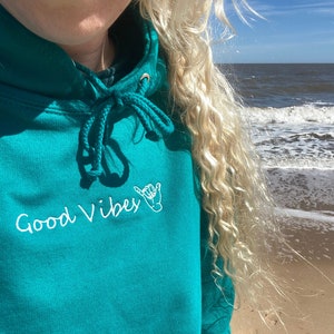 May include: Teal blue hoodie with a white embroidered design that says "Good Vibes" with a hand gesture.