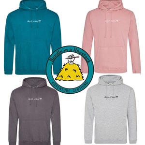 May include: Five hooded sweatshirts in different colors, including teal, pink, gray, and charcoal. Each sweatshirt has the text "Good Vibes" and a small hand gesture graphic printed on the front. The sweatshirts are arranged in a circle around a logo that reads "Needle in a Haystack Adventure Clothing".