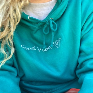 May include: Teal blue hoodie with a white embroidered design that says "Good Vibes" with a hand gesture.