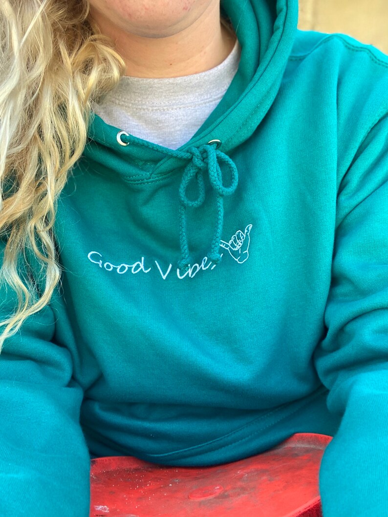 May include: Teal blue hoodie with a white embroidered design that says "Good Vibes" with a hand gesture.