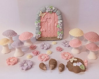 May include: A collection of fairy garden decorations, including a pink door with a heart cutout, colorful mushrooms, flowers, hedgehogs, and a tree stump. The items are in pastel colors and are likely made of a decorative material.