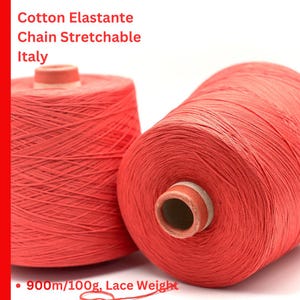 May include: Two spools of coral red cotton elastane chain stretchable yarn. The text on the image reads: Cotton Elastante, Chain Stretchable, Italy, 900m/100g, Lace Weight. The yarn is wound tightly around cylindrical cores for textile use.