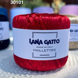 May include: A vibrant red ball of Lana Gatto Paillettes yarn featuring a white paper label with the text 30101, Lana Gatto, Made in Italy, and Paillettes. The yarn has a shiny, metallic texture with small, reflective sequins integrated throughout.