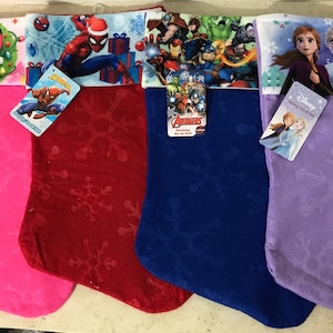 Puede incluir: Cuatro calcetines de Navidad con diferentes temas de personajes de Disney. Los calcetines son rosa, rojo, azul y morado con un patrón de copo de nieve. Los personajes que aparecen son Mickey Mouse y Minnie Mouse, Spiderman, los Vengadores y Frozen.