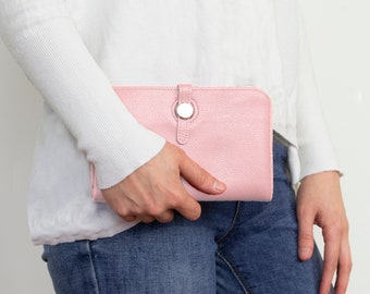 以下が含まれることがあります： 銀色のボタン留め具が付いたピンクの革財布。財布は、白いセーターと青いジーンズを着た人が持っています。