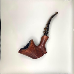 May include: A handcrafted tobacco pipe with a curved stem and a dark brown finish. The bowl is a lighter shade of brown with a unique, organic shape. The pipe is made of wood and has a smooth, polished appearance.