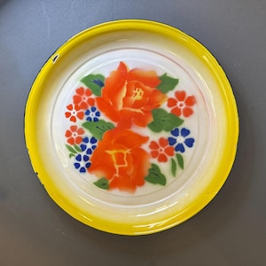 Puede incluir: Una bandeja redonda con borde amarillo e interior blanco. La bandeja presenta un diseño floral con rosas naranjas, flores rojas y azules y hojas verdes. La bandeja es probablemente de metal.
