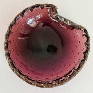 May include: A plum-coloured, hand-blown glass bowl. The bowl has a textured surface with small bubbles. The rim is trimmed with a gold-toned edge. This decorative piece would make a lovely addition to any home, measuring approximately 20 cm in diameter.
