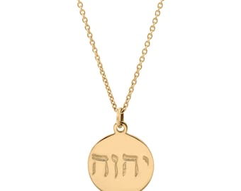 May include: A gold-toned necklace featuring a circular pendant suspended from a delicate chain. The pendant is engraved with four Hebrew characters across its centre, displaying a smooth, polished finish on the metal surface.