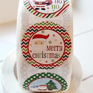 May include: Roll of round Christmas stickers with a red, green and white colour scheme. The stickers feature a cartoon Santa Claus, a Christmas tree, and the text "Ho Ho Ho" and "Merry Christmas".