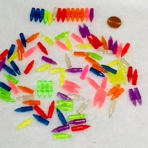 May include: A collection of small, colorful, bullet-shaped plastic beads in various colors, including blue, green, red, orange, and purple. A penny is also present. These beads could be used for crafts or jewelry making.