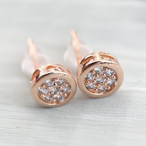 Peut inclure: Une paire de boucles d'oreilles clous en or rose avec de petits sertis ronds remplis de pierres de zircone cubique transparentes.