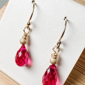 Peut inclure: Une paire de boucles d'oreilles en or avec des pierres précieuses rouges en forme de goutte et des perles dorées.
