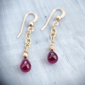May include: A pair of gold dangle earrings with a teardrop-shaped red gemstone and a chain of small gold beads.