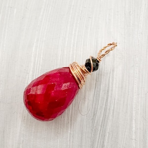 Peut inclure: Un pendentif fait à la main avec une pierre précieuse rouge en forme de goutte d'eau facettée. La pierre est enveloppée de fil de cuivre, et une petite perle noire est également incorporée. Le pendentif a une boucle torsadée en fil de cuivre pour l'accrocher.