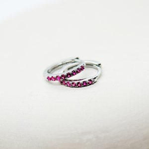 Può includere: Un paio di orecchini a cerchio d'argento con una fila di pietre preziose rosa attorno al bordo.