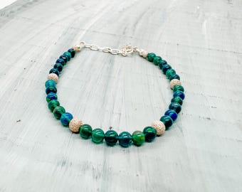 May include: A green and blue beaded necklace with silver accents. The necklace is made of round beads with a textured surface.